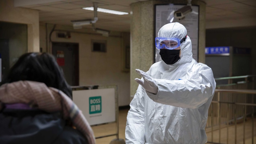 Worker in hazardous materials suit stops a passenger in the Beijing subway.