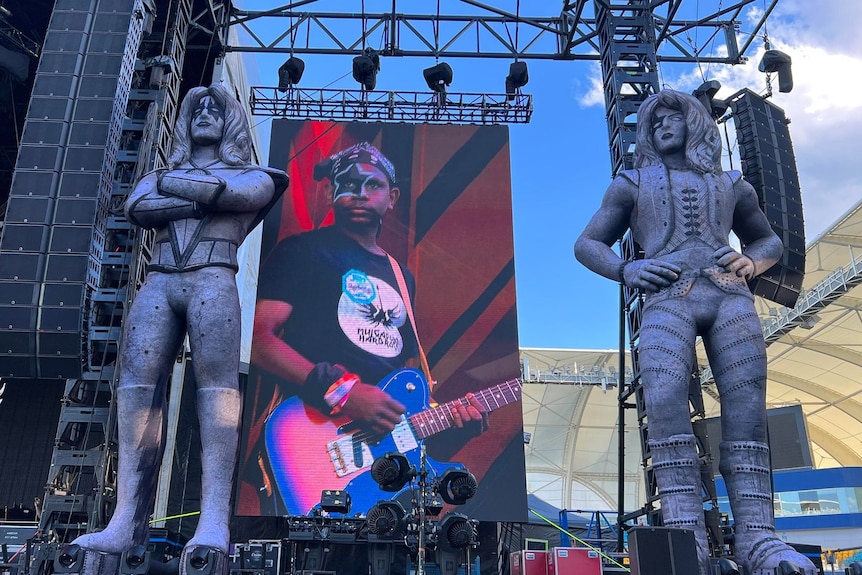 Big Screen surrounding by rigging and oversized statues of KISS band members
