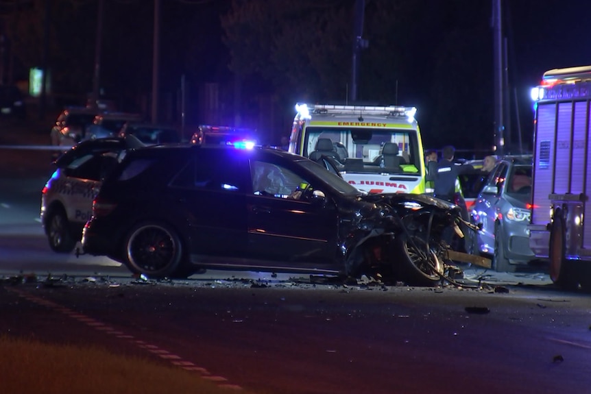 An ambulance behind a damaged Mercedes on a road at night.