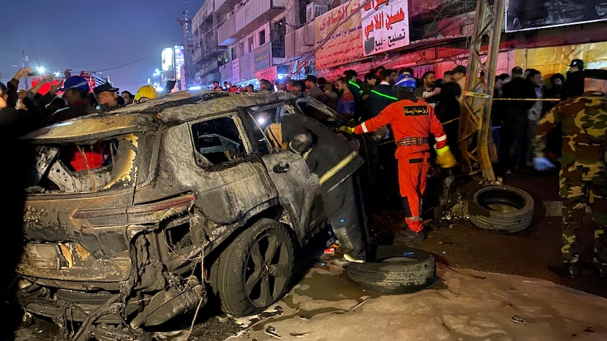 A civil defence member gathers around a burned vehicle that was targeted by a US drone strike in Baghdad.