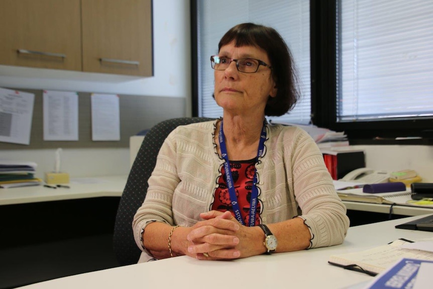 State School Teachers' Union of WA president Pat Byrne sits at her desk in an office with her arms clasped in front of her.