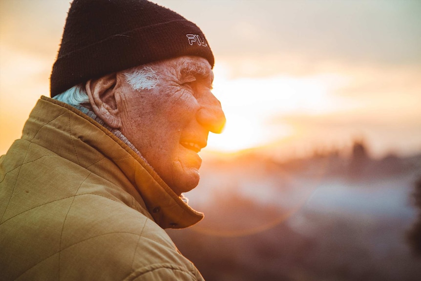 Older man in a beanie smiling against the sunset or dawn