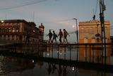 people walk over a flooded street between two buildings.