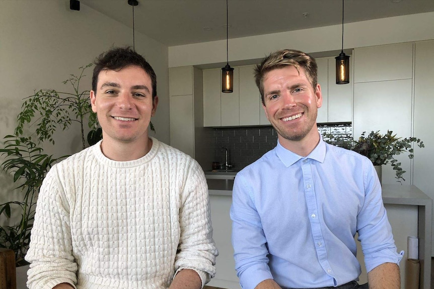 Two men siting in their apartment smiling at the camera