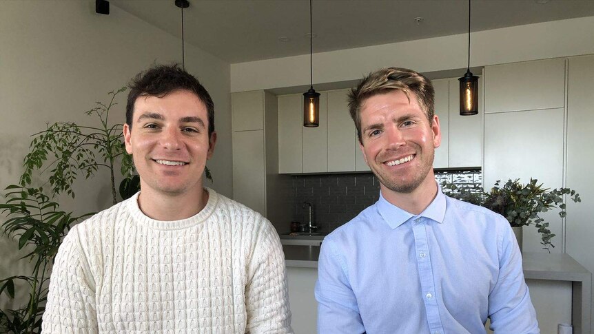 Two men siting in their apartment smiling at the camera