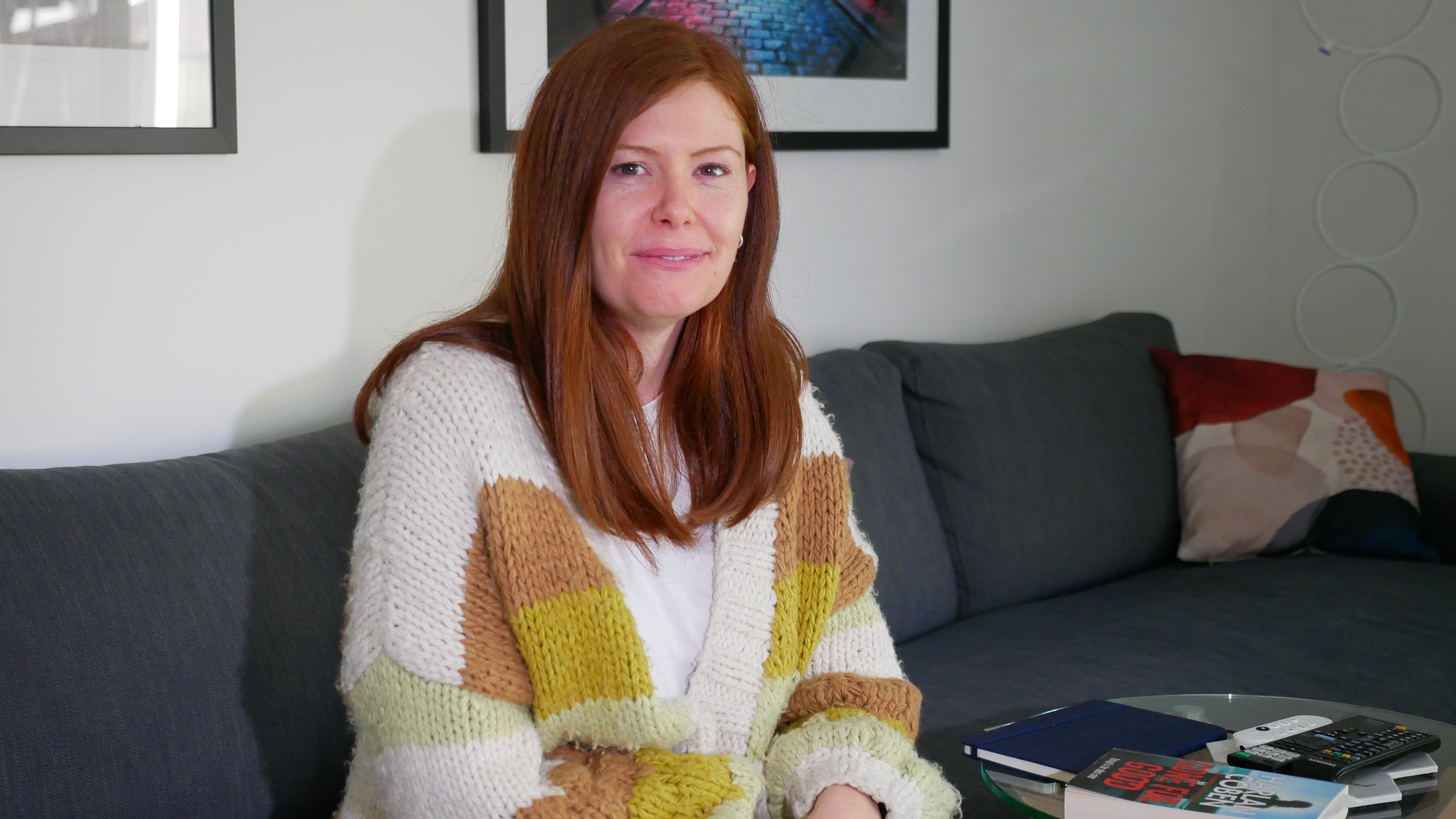 A red-haired woman wearing a yellow striped sweater sitting on a grey couch
