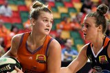 A WNBL basketballer holds the ball and looks around for a teammate while an opponent guards her.