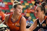 A WNBL basketballer holds the ball and looks around for a teammate while an opponent guards her.