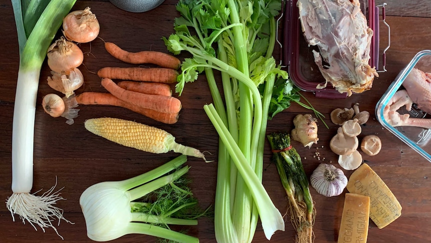 Leek, onion, carrots, corn, fennel, celery, herbs, garlic, ginger, mushrooms and chicken bones on a table, stock ingredients.