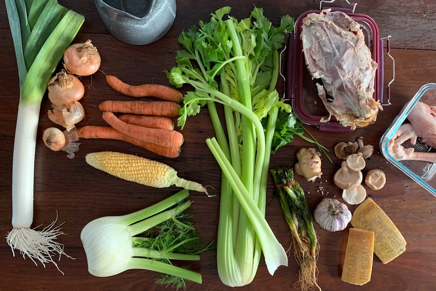 Leek, onion, carrots, corn, fennel, celery, herbs, garlic, ginger, mushrooms and chicken bones on a table, stock ingredients.