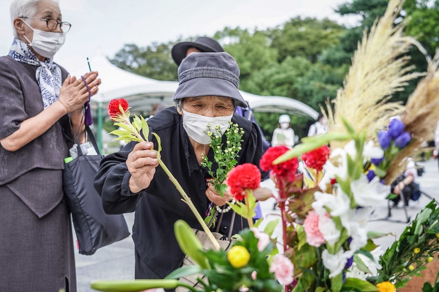 An elderly woman lays flowers at the Hiroshima Peace Memorial Ceremony