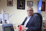 Man in a navy blue suit sitting at a desk 