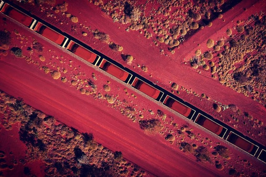 An aerial photo of an iron ore train surrounded by the red dirt of the Pilbara in Western Australia