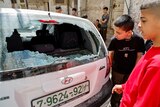 Children look through the smashed window of small white hatchback.