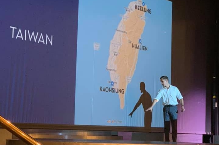 A man on a stage in front of a projection of a map of Taiwan