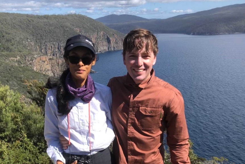 Woman and man in hiking gear with rocky cape and water in the background