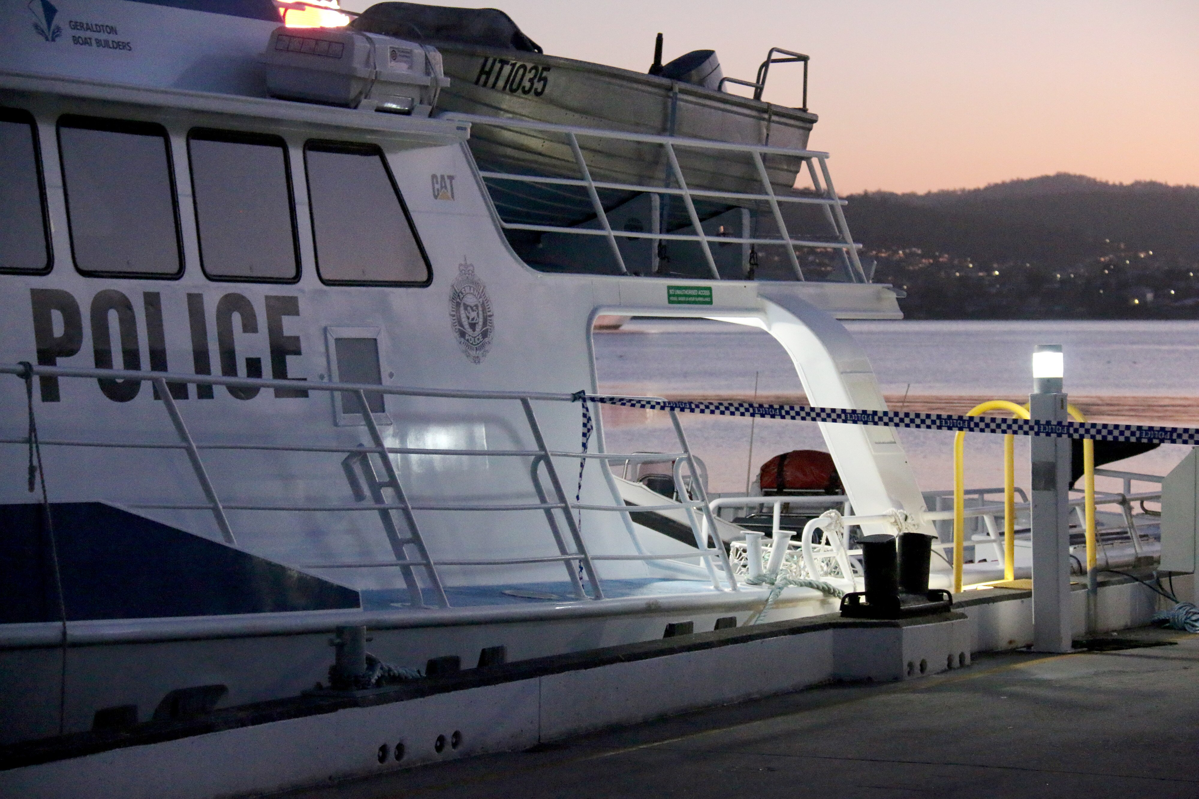 A boat with police written across it and police tape along a wharf stopping anyone getting too close