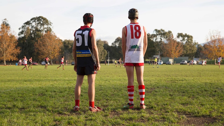 Two opposing footballers wearing helmets stand apart on a field.