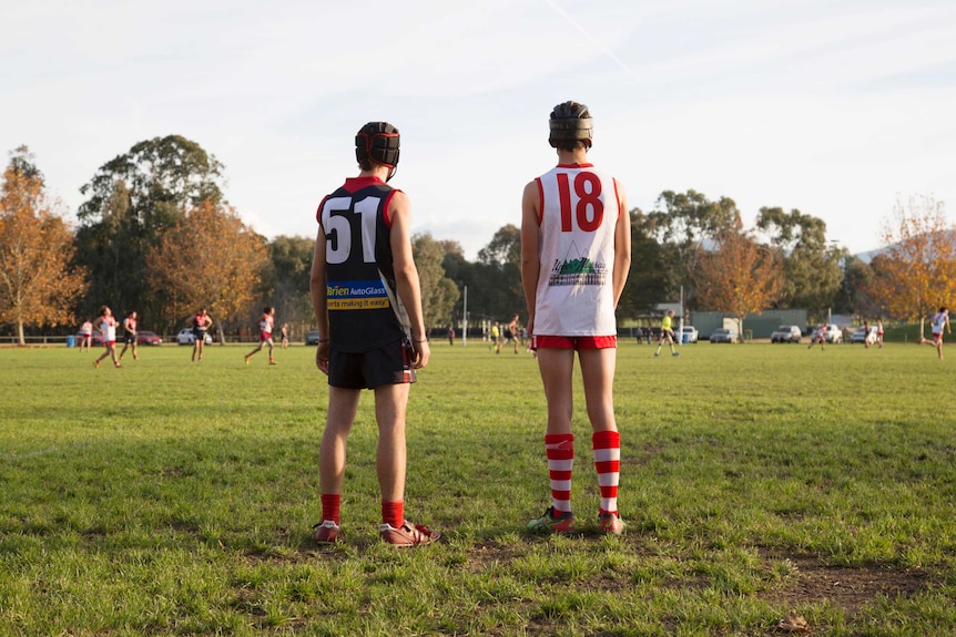 Two opposing footballers wearing helmets stand apart on a field.