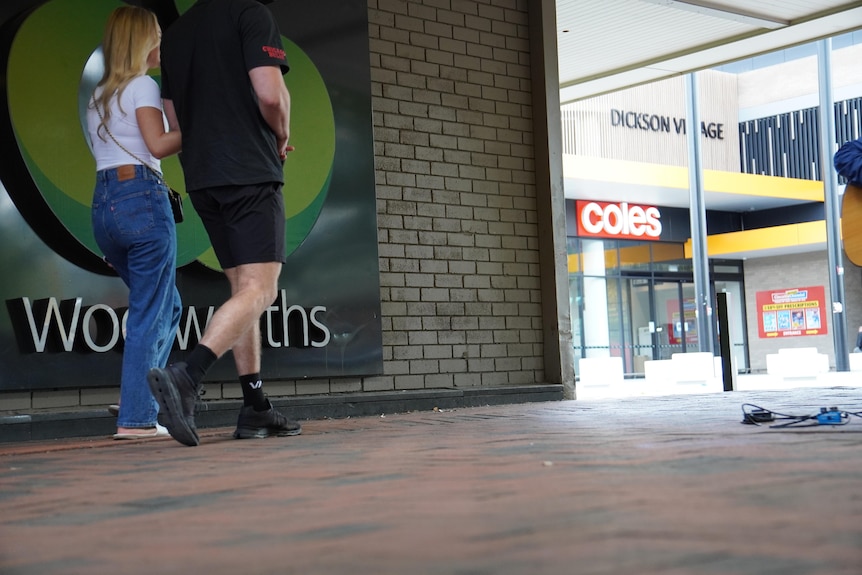 Customers walking past Coles and Woolworths branding outside neighbouring supermarkets