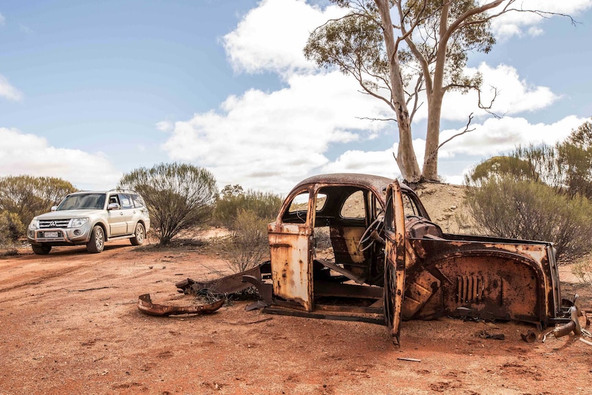 A four-wheel-drive moving past a rusted out car in the bush