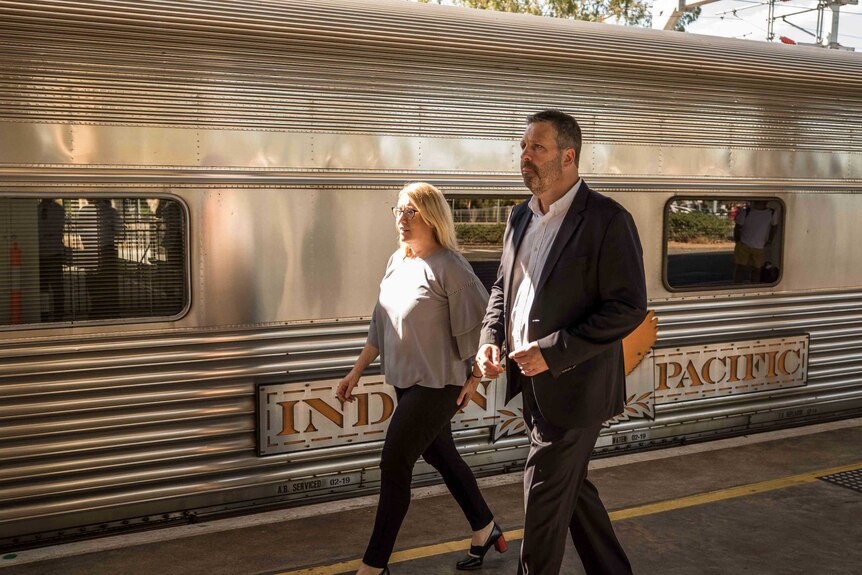 A woman and a man walking on a train platform next to a carriage.