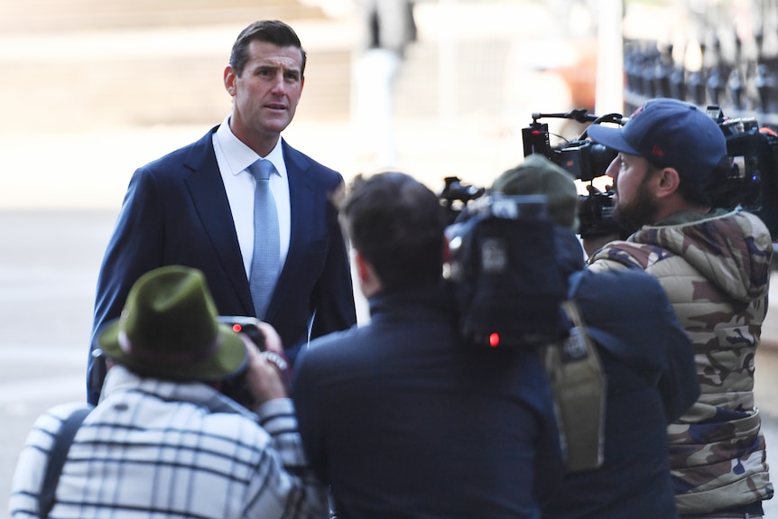 a man wearing a suit standing in front of video and photo cameras