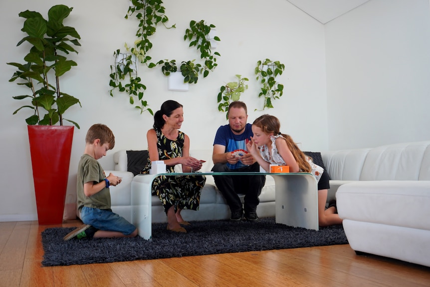 A family of four sitting in their lounge room, a plant wall is behind them.