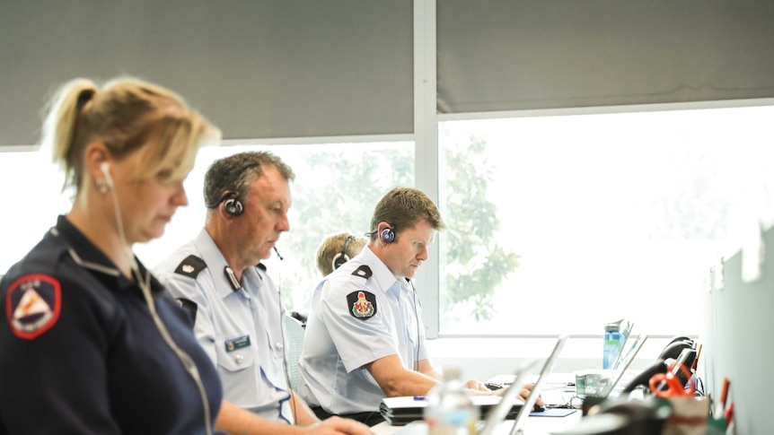 One female and two male paramedics sit at desks, looking at laptops.