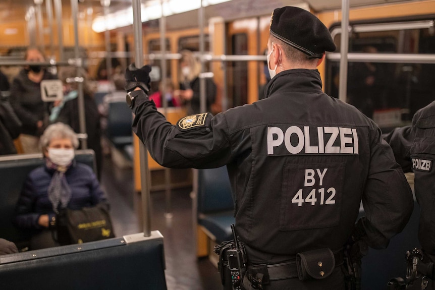 A police officer wearing a hat and a mask looks out over a bus with passengers wearing masks