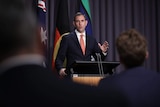 A man in a suit and tie speaks to seated media in Parliament House's Blue Room.
