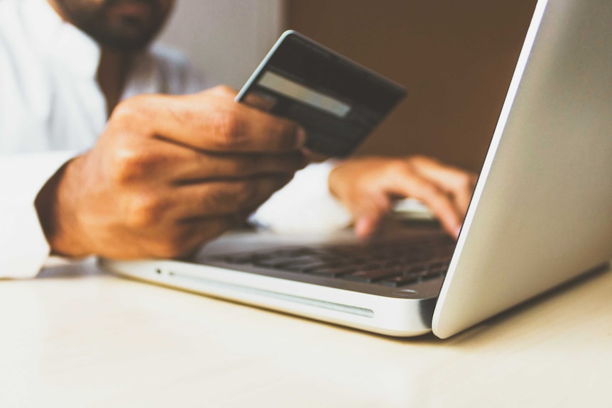 A man holds a credit card in front of a laptop