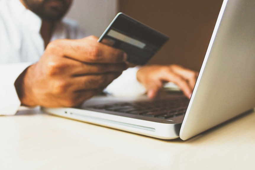 A close up of a man's hand holding an obscured credit card while the other hand types on a laptop.