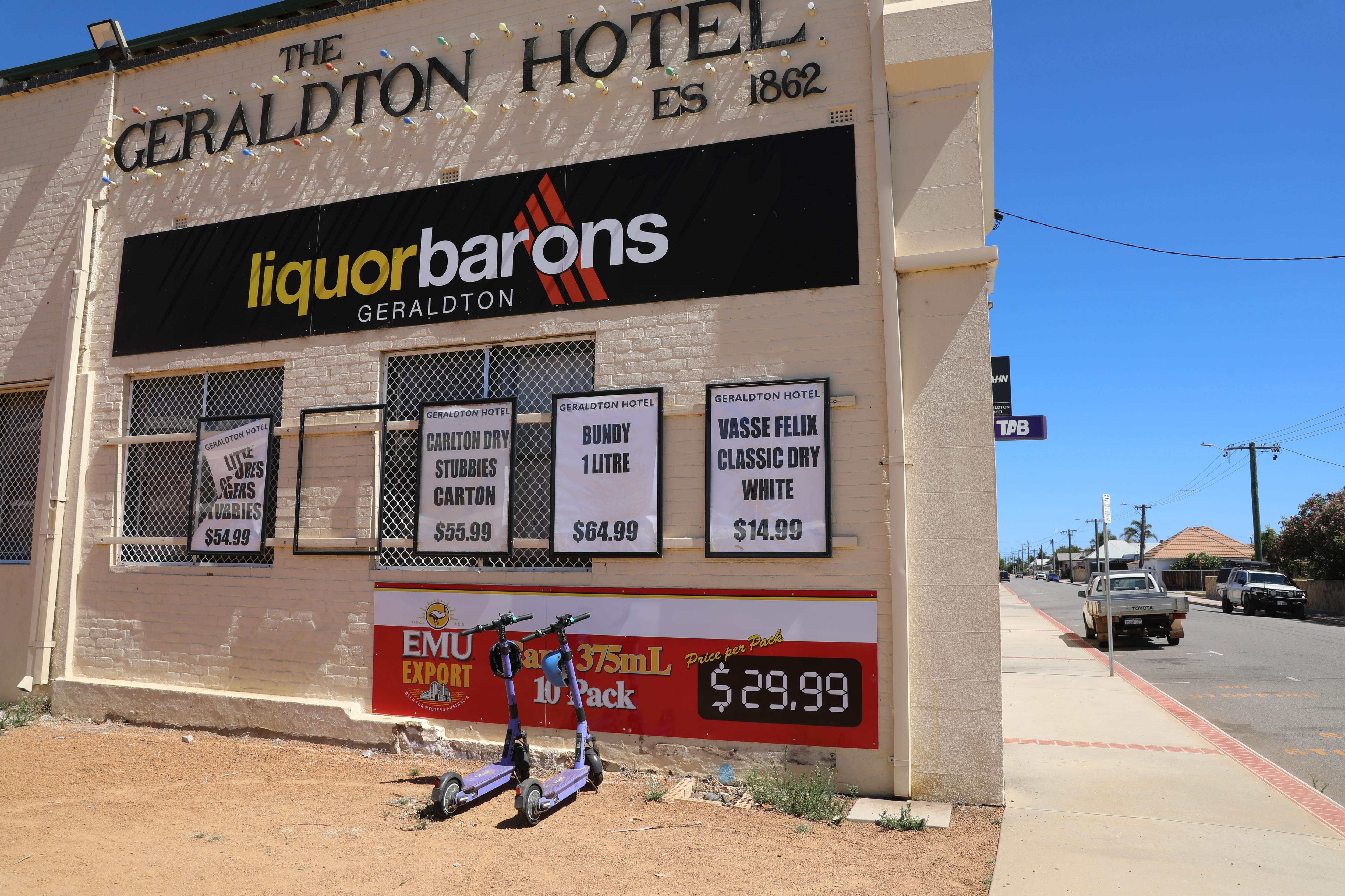 Dos patinetes eléctricos estacionados frente a un edificio con un cartel que dice “ "barones del alcohol".