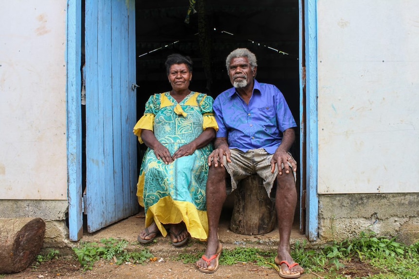 A woman and a man in bright island-style clothes sit for a portrait.