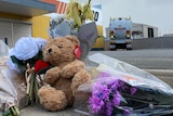 A teddy bear and flowers with a garbage truck parked behind