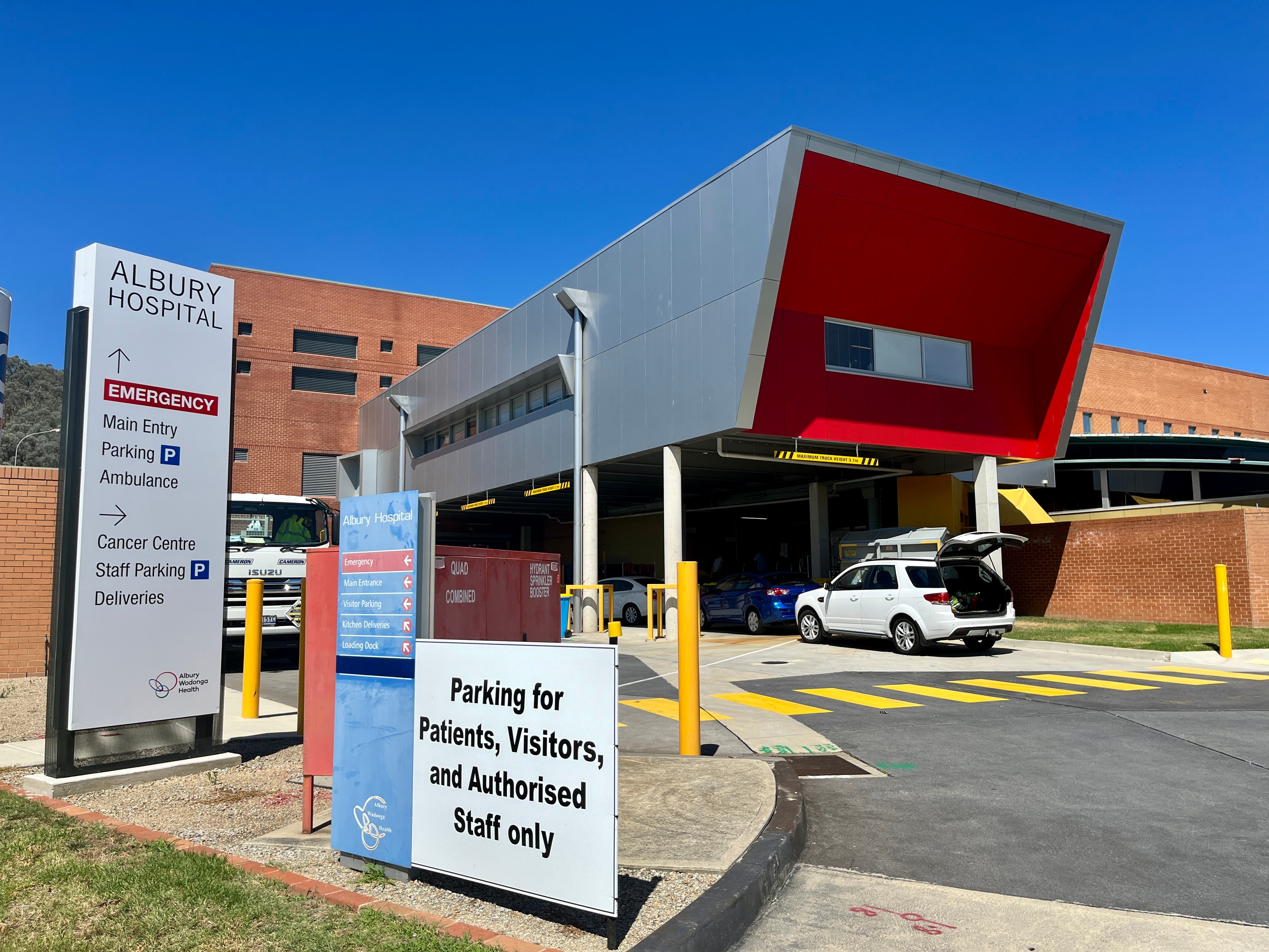 A front view of the Albury Wodonga hospital, a sign directs to the emergency department, car park and cancer centre.