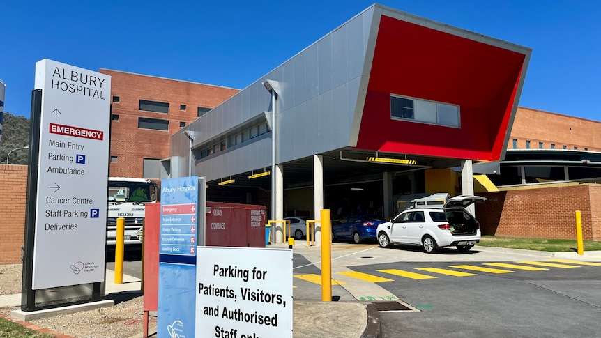 A front view of the Albury Wodonga hospital, a sign directs to the emergency department, car park and cancer centre.