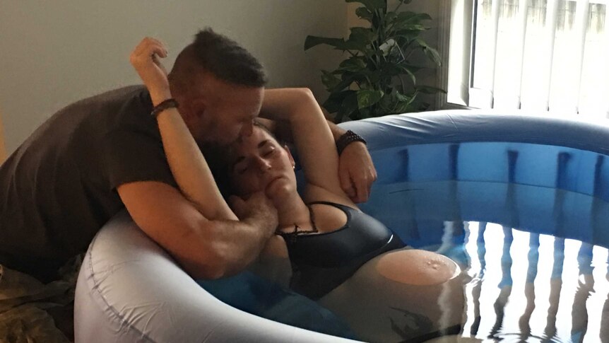 Steve Kleidon comforts his wife Krystal as she sits in the inflatable pool in their living room