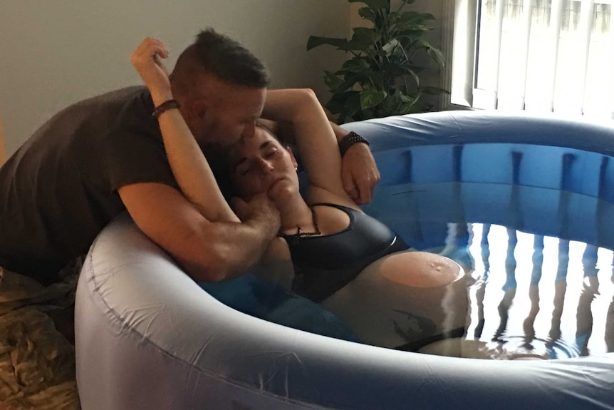 Steve Kleidon comforts his wife Krystal as she sits in the inflatable pool in their living room