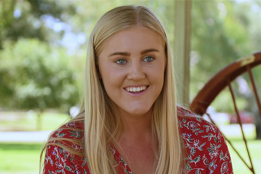 A blonde woman smiles in front of the camera.