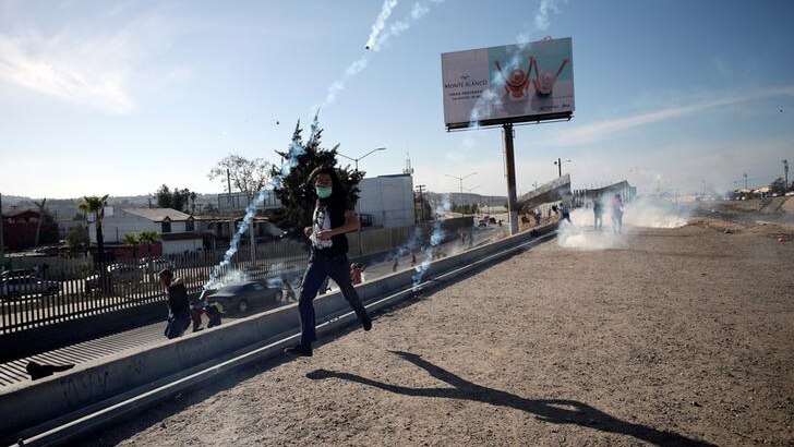 A migrant runs away from approaching tear gas canisters with a covered face along US-Mexico border