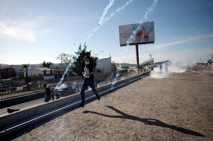 A migrant runs away from approaching tear gas canisters with a covered face along US-Mexico border