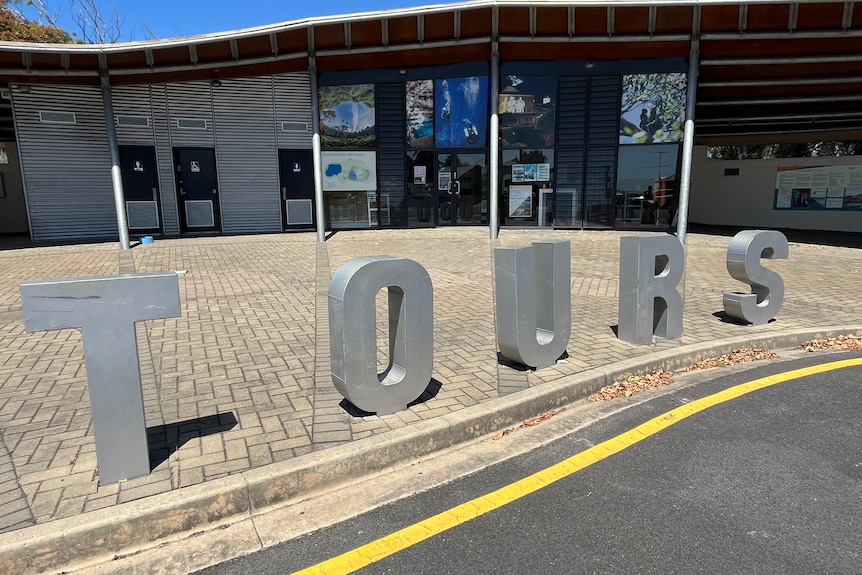 A modern building with metal letters on pavement spelling "TOURS".