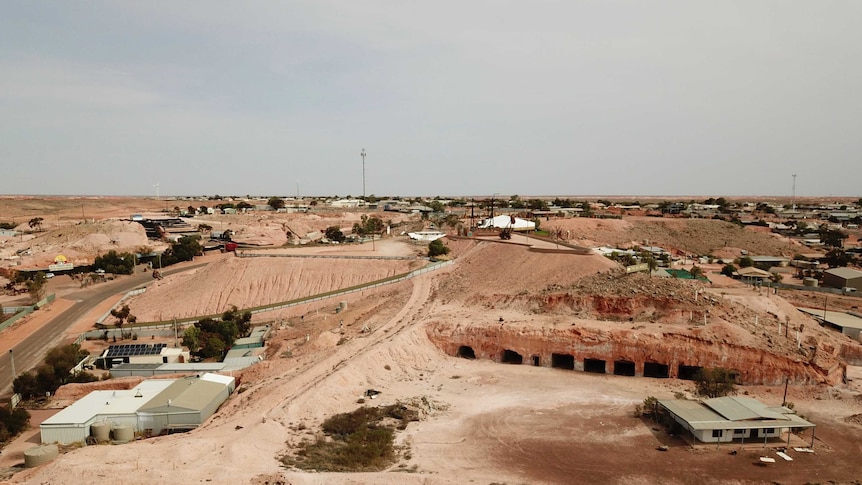 Houses dot along small rolling red dirt hills against a blue-grey background.