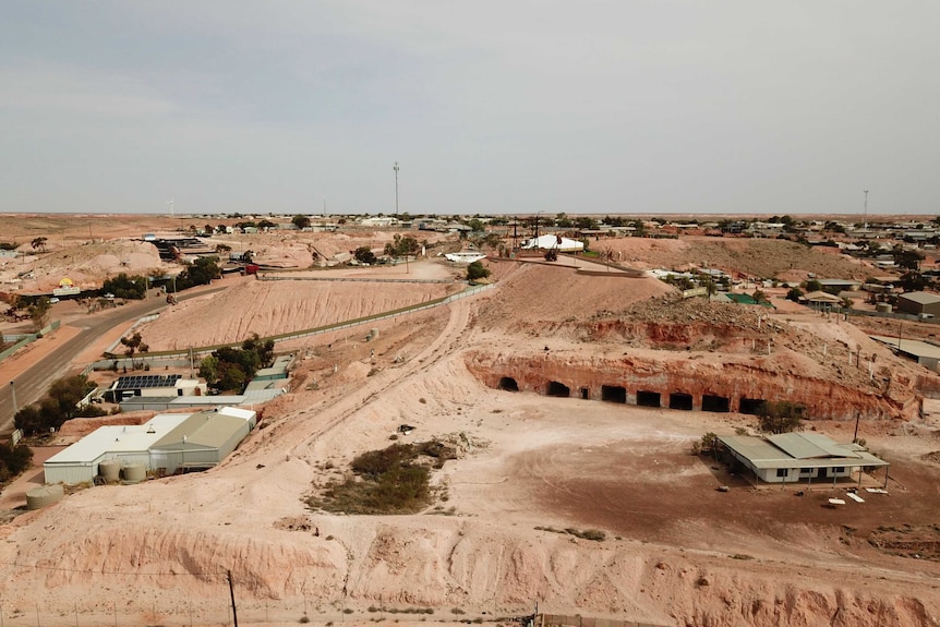 Houses dot along small rolling red dirt hills against a blue-grey background