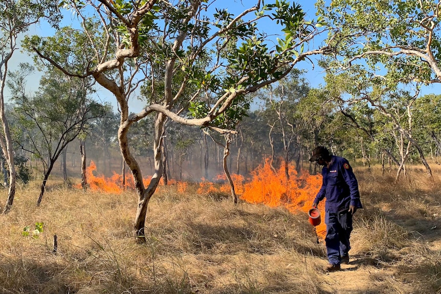 A man in Mimal rangers uniform burns a line in the grass with a fuel cannister in his hand.