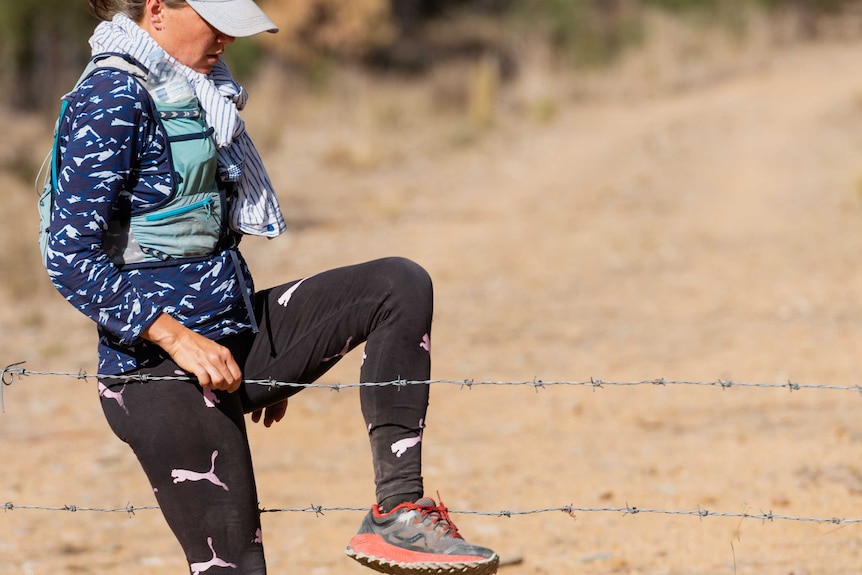 Jess steps over a barbed wire fence during the obstacle course.