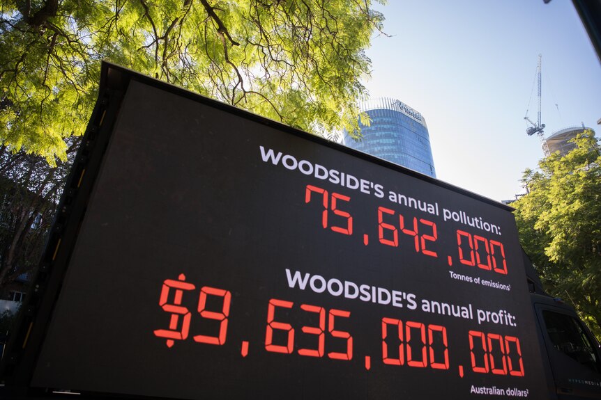 A truck comparing Woodside's annual pollution to its profit underneath the Woodside building.