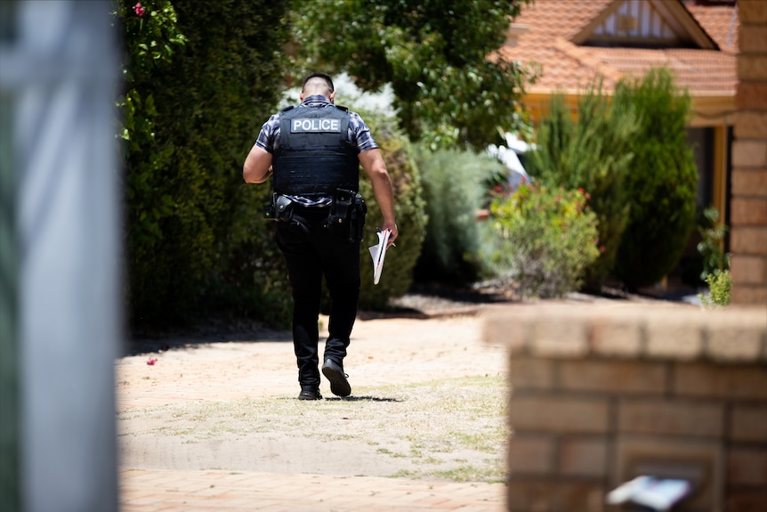 A police officer in a bullet-proof vest walks with his back turned to the camera.